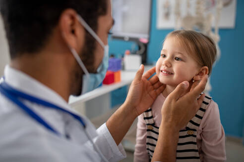 Ein junger Arzt untersucht in seiner Praxis die Lymphknoten eines kleinen Mädchens. - HPIF01152