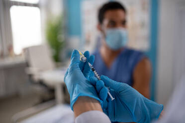 A close-up of doctor holding covid-19 vaccince syringe and preparing to give it to her colleague. - HPIF01157