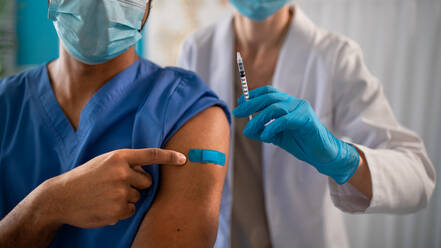 A close-up of unrecognizable doctor showing bandage on his arm after vaccince. - HPIF01161