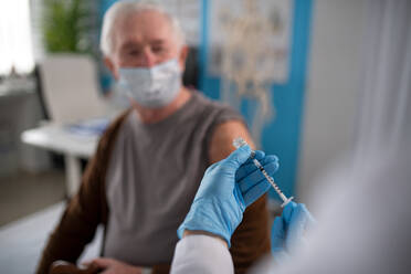 A close-up of doctor holding covid-19 vaccince syringe and preparing to give it to senior man. - HPIF01168