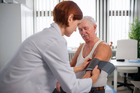 Eine Ärztin misst den Blutdruck eines älteren männlichen Patienten in ihrer Praxis. - HPIF01174