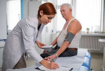 A female doctor measuring blood pressure to senior man patient in her office. - HPIF01175