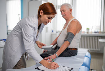 Eine Ärztin misst den Blutdruck eines älteren männlichen Patienten in ihrer Praxis. - HPIF01175