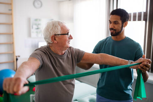 Eine junge Physiotherapeutin trainiert mit einem älteren Patienten in einem Behandlungsraum - HPIF01188