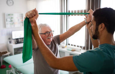 A young physiotherapist exercising with senior patient in a physic room - HPIF01189