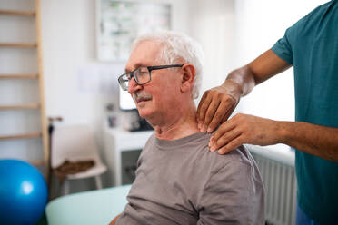 Eine junge Physiotherapeutin massiert den Nacken eines älteren Patienten in einem Krankenzimmer - HPIF01191