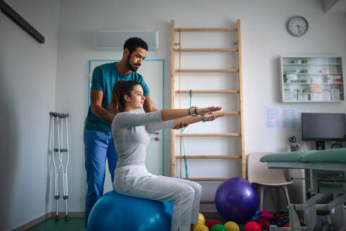 Ein junger männlicher Physiotherapeut trainiert mit einer jungen Patientin in einem Behandlungsraum - HPIF01201