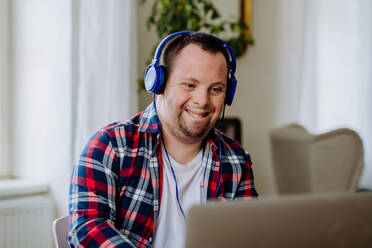 Ein junger Mann mit Down-Syndrom sitzt am Schreibtisch im Büro, benutzt einen Laptop und hört Musik über Kopfhörer. - HPIF01203