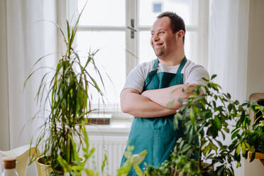 Junger Mann mit Down-Syndrom, der sich um Pflanzen kümmert und als Verkäufer in einem Blumenladen arbeitet. - HPIF01207