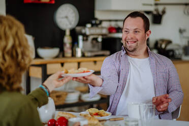 Ein Porträt eines glücklichen Mannes mit Down-Syndrom und seiner Mutter beim gemeinsamen Frühstück zu Hause. - HPIF01208