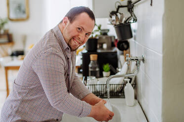 Ein Mann mit Down-Syndrom wäscht das Geschirr, kümmert sich um sich selbst, Konzept der Unabhängigkeit und sozialen Integration. - HPIF01211