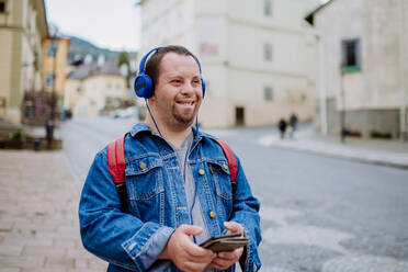 Ein glücklicher junger Mann mit Down-Syndrom, der beim Gehen auf der Straße Musik hört. - HPIF01213