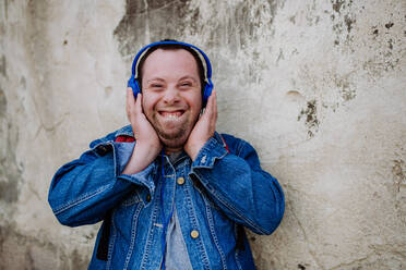 A close-up portrait of happy young man with Down sydrome listening to music when walking in street. - HPIF01216