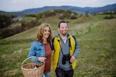 Ein Porträt eines glücklichen jungen Mannes mit Down-Syndrom und seiner Mutter, die gemeinsam in der Natur wandern. - HPIF01218