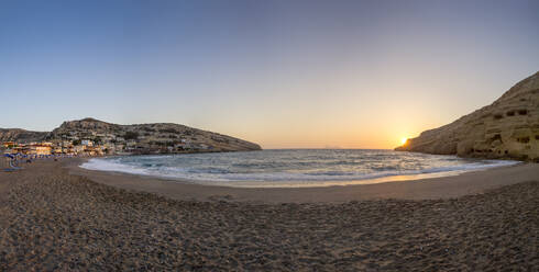 Griechenland, Kreta, Matala, Panoramablick auf den Strand von Matala bei Sonnenuntergang mit Dorf im Hintergrund - MAMF02315