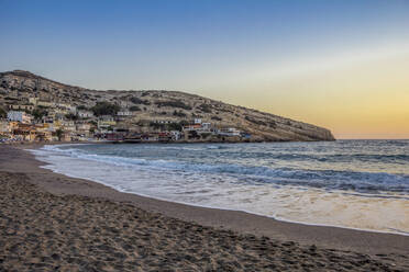 Griechenland, Kreta, Matala, Matala Strand in der Abenddämmerung mit Dorf im Hintergrund - MAMF02323