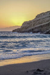 Greece, Crete, Matala, Matala Beach and cliffside caves at sunset - MAMF02324