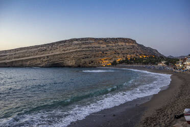 Greece, Crete, Matala, Matala Beach and cliffside caves at dusk - MAMF02325