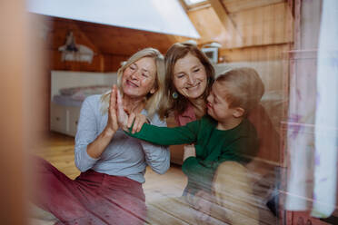 Ein Junge mit Down-Syndrom mit seiner Mutter und Großmutter, die zu Hause sitzen und durch das Fenster schauen. - HPIF01247