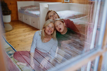 A boy with Down syndrome with his mother and grandmother sitting and looking through window at home. - HPIF01249