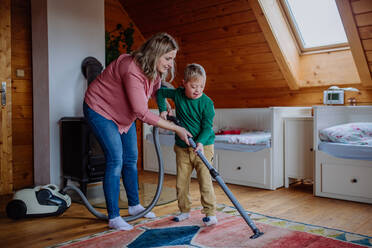 Ein Junge mit Down-Syndrom und seine Mutter beim Staubsaugen zu Hause - HPIF01266