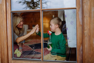 Ein Junge mit Down-Syndrom putzt zusammen mit seiner Großmutter zu Hause die Fenster. - HPIF01269