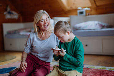 Ein Kind mit Down-Syndrom sitzt auf dem Boden und benutzt mit seiner Großmutter zu Hause ein Tablet. - HPIF01273