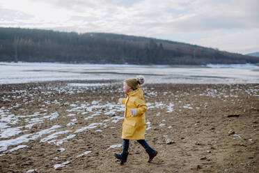 Ein glücklicher kleiner Junge mit Daunen, der im Winter draußen am See läuft. - HPIF01292