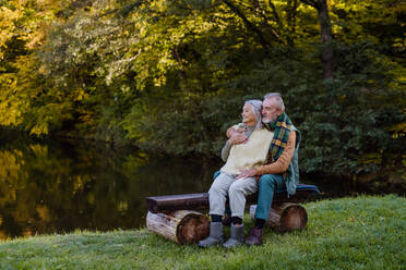 Verliebtes älteres Paar sitzt zusammen auf einer Bank in der Nähe eines Sees, während eines Herbsttages. - HPIF01334