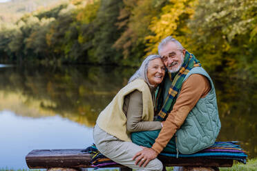 Verliebtes älteres Paar sitzt zusammen auf einer Bank in der Nähe eines Sees, während eines Herbsttages. - HPIF01336