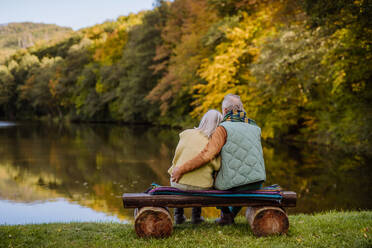 Verliebtes älteres Paar auf einer Bank sitzend, mit Blick auf einen See, an einem Herbsttag, Rückansicht. - HPIF01339