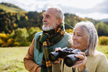 Älteres Paar betrachtet die Aussicht durch ein Fernglas auf einem Herbstspaziergang. - HPIF01358
