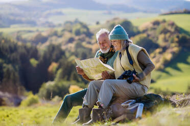 Senior couple having a break, lookig into paper map during hiking in autumn nature. - HPIF01359