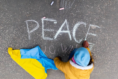 A top view of little girl writing peace with chalk. Protest against Russian invasion of Ukraine. - HPIF01414