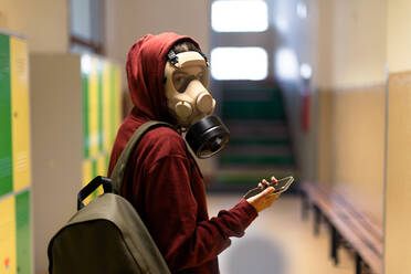 Ein junger Schüler mit Gasmaske und Smartphone in der Schule. - HPIF01432