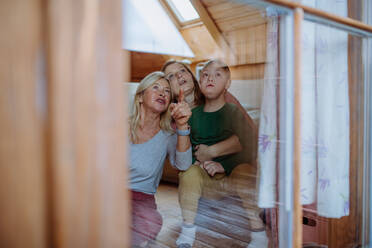 A boy with Down syndrome with his mother and grandmother sitting and looking through window at home. - HPIF01435