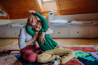 Ein glücklicher Junge mit Down-Syndrom, der auf dem Boden sitzt und sich mit seiner Großmutter zu Hause umarmt - HPIF01439