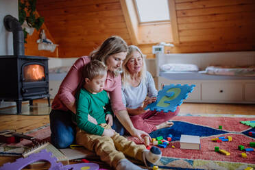 Ein Junge mit Down-Syndrom sitzt auf dem Boden und spielt mit seiner Mutter und Großmutter zu Hause - HPIF01440