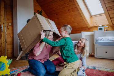 Ein Junge mit Down-Syndrom spielt mit seiner Mutter und seiner Großmutter zu Hause mit einer Schachtel. - HPIF01441