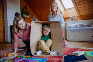 A boy with Down syndrome with his mother and grandmother playing with box together at home. - HPIF01442