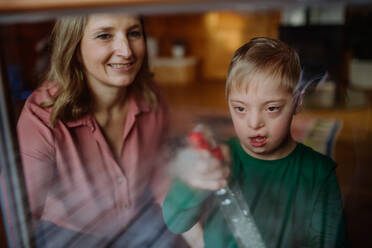 Ein Junge mit Down-Syndrom und seine Mutter beim Fensterputzen zu Hause. - HPIF01446
