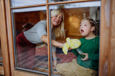 Ein Junge mit Down-Syndrom mit seiner Mutter und Großmutter beim Fensterputzen zu Hause. - HPIF01447