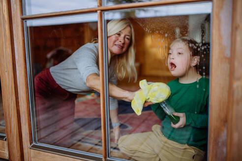 Ein Junge mit Down-Syndrom mit seiner Mutter und Großmutter beim Fensterputzen zu Hause. - HPIF01447