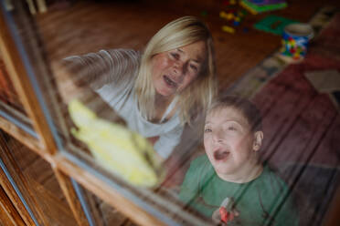 Ein Junge mit Down-Syndrom mit seiner Mutter und Großmutter beim Fensterputzen zu Hause. - HPIF01448