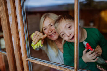 A boy with Down syndrome with his mother and grandmother cleaning window at home. - HPIF01449