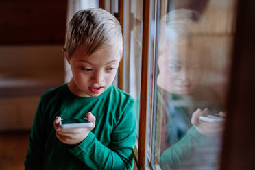 Ein trauriger kleiner Junge mit Down-Syndrom benutzt sein Smartphone zu Hause - HPIF01454