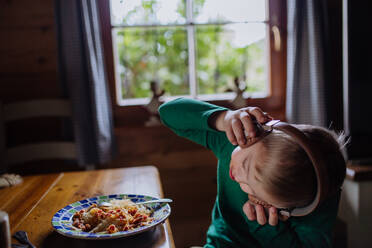 Ein Junge mit Down-Syndrom isst zu Hause mit Kopfhörern zu Mittag und schaut in die Kamera. - HPIF01456