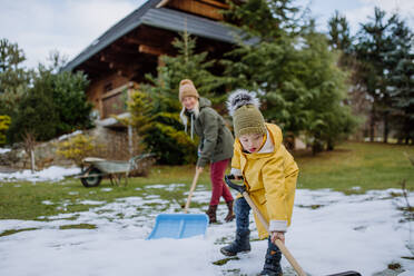 Ein Junge mit Down-Syndrom und seine Mutter räumen mit einer Schaufel den Schnee vom Weg vor dem Haus. - HPIF01460