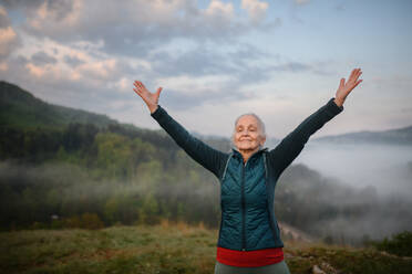Eine ältere Frau macht Atemübungen in der Natur am frühen Morgen mit Nebel und Bergen im Hintergrund. - HPIF01517
