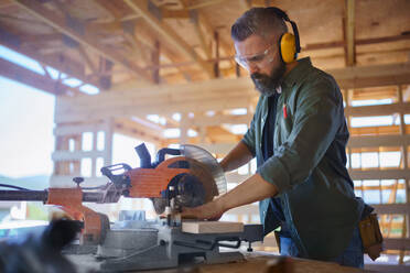 Construction worker working with eletric saw inside a wooden construction of house, diy eco-friendly homes concept. - HPIF01523